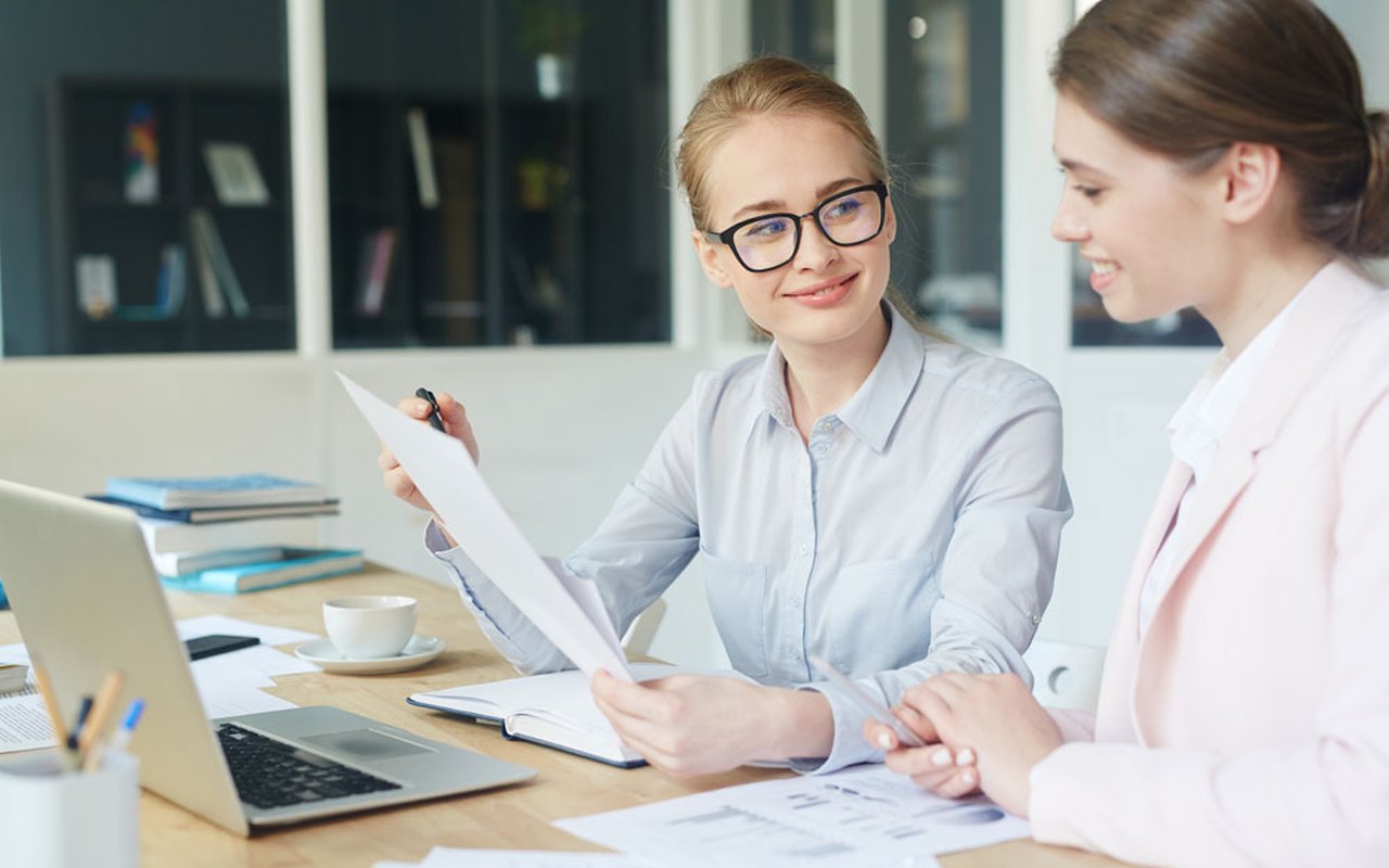 Two colleagues reviewing documents at a desk during office and business communication training